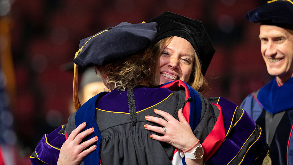Graduate student at commencement hugging professor