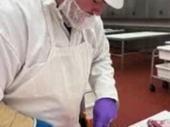Meat Butcher with proper safety gear slicing meat