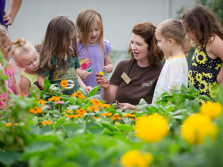 Children gathered around adult teacher in a field of flowers